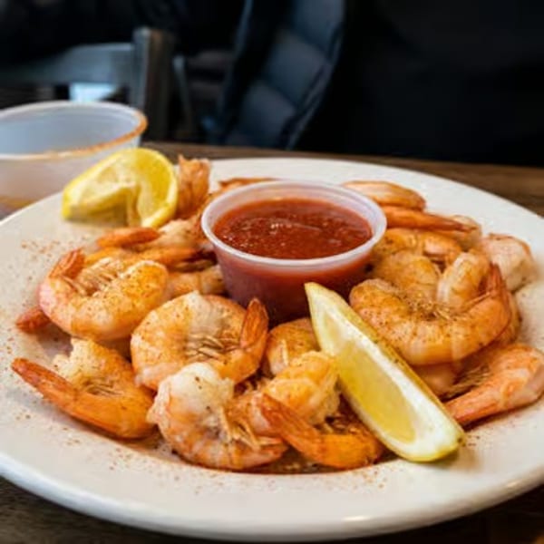 A plate of seasoned shrimp with cocktail sauce and lemon wedges.
