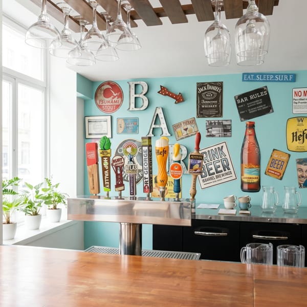 A bar with beer taps, a wooden counter, and a light blue wall decorated with various beer signs.
