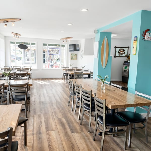 Bright, empty restaurant dining room with wooden tables, black chairs, and a turquoise accent wall.