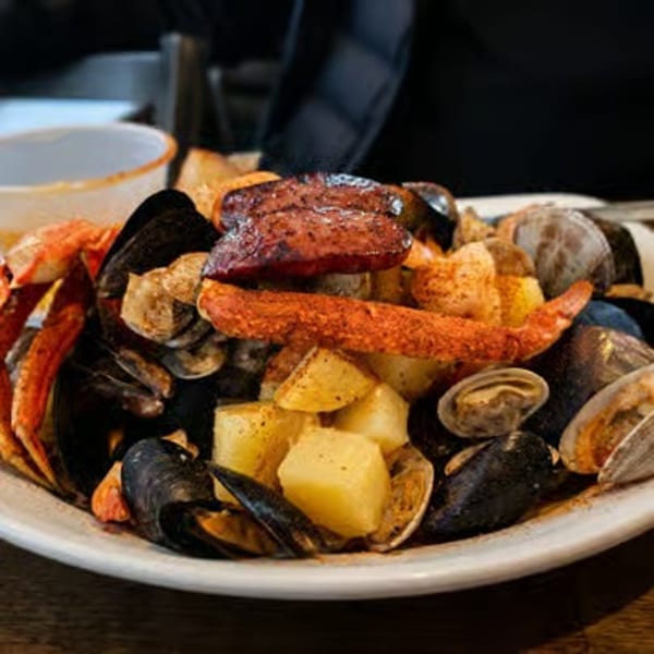 A seafood boil with crab legs, mussels, clams, sausage, and potatoes on a white plate.