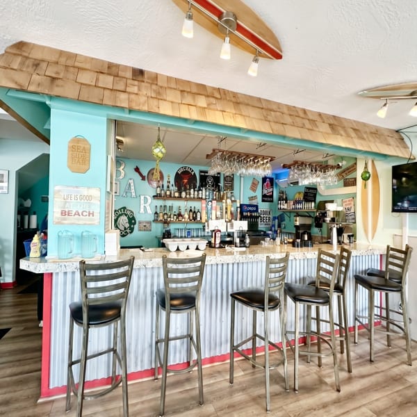 A vibrant bar with a teal wall, corrugated metal counter, and surf-themed decor.