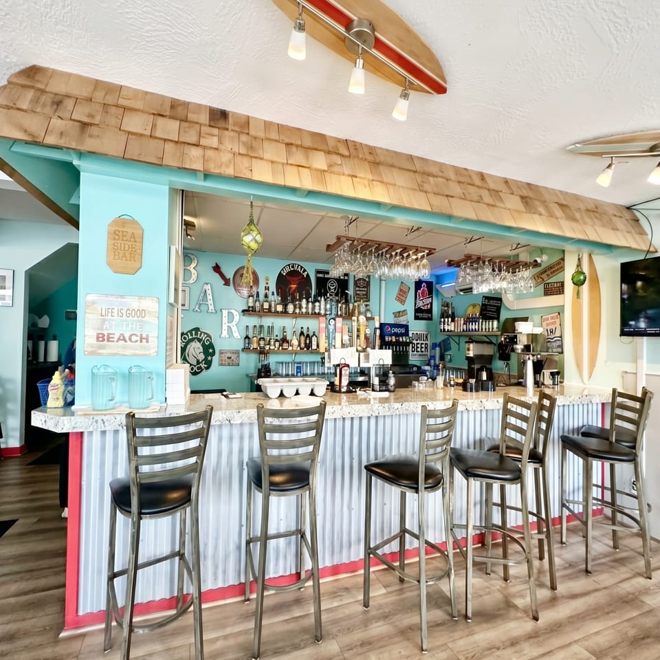 A vibrant bar with a teal wall, corrugated metal counter, and surf-themed decor.
