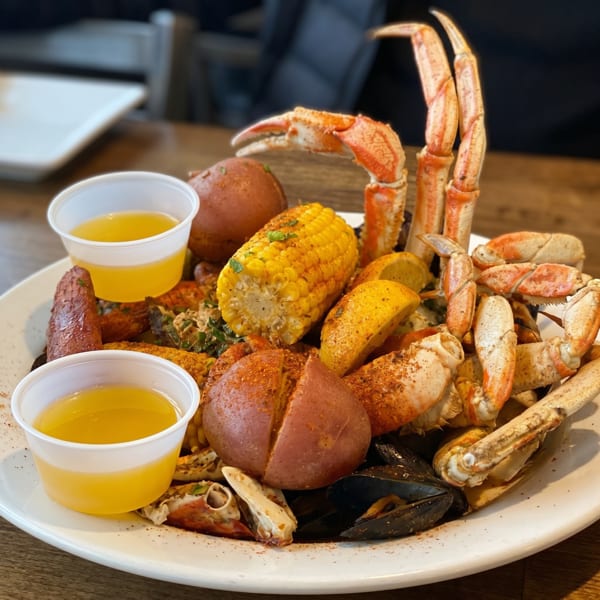 A seafood boil with crab legs, corn on the cob, potatoes, mussels, and two cups of butter.
